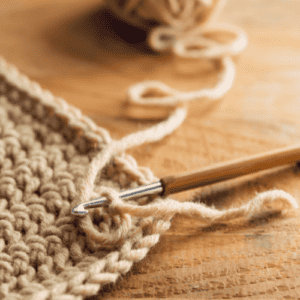 Crochet hook laying on top of tan yarn swatch